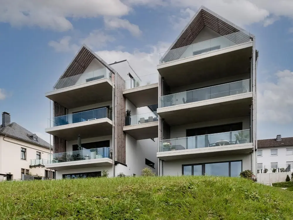 Atriumhaus in Gummersbach-Hülsenbusch: zwei weiße Giebelhäuser mit Glasbrüstungen und seitlichen Holzlamellen, von der Talseite gesehen