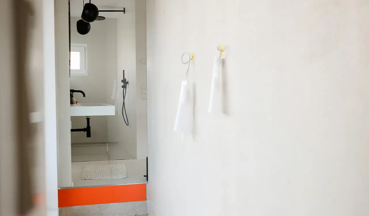 Bad mit offener Dusche, orangefarbenem Akzent und hellen Wandflächen