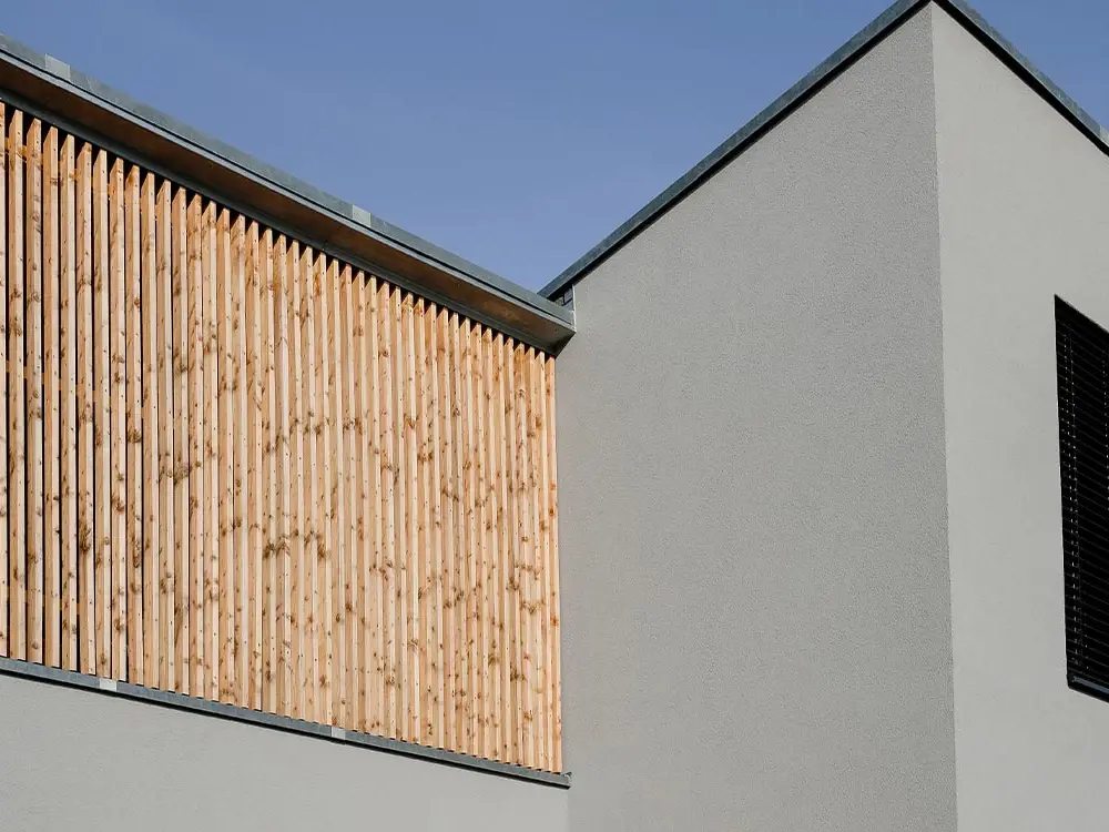 Fassade von Mi49 mit vertikalen Holzlamellen über weißem Putz vor blauem Himmel