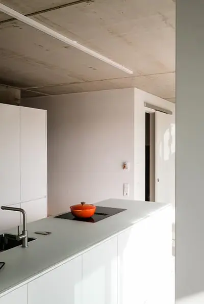 Küche zwischen Sichtbetonwand und weißen Einbauten