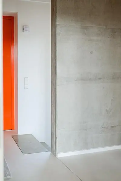 Orangefarbene Tür neben einer Sichtbetonwand